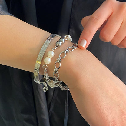 Young woman wearing the Perla Héritage bracelet stack featuring an engraved polished Stainless Steel bangle, pearl bracelet, and sculptural chain bracelet.