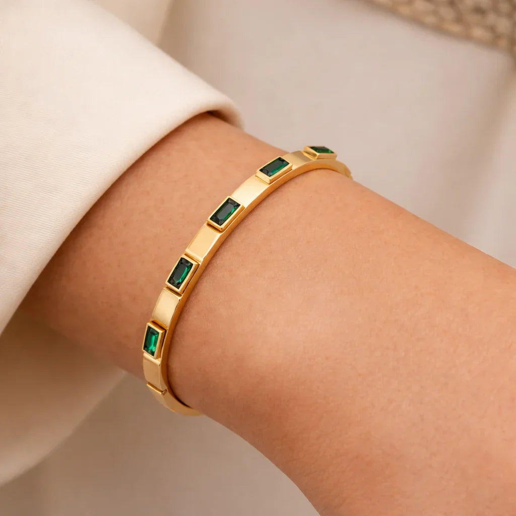 Emerald baguette gold bangle bracelet on wrist, satin finish with green baguette stones