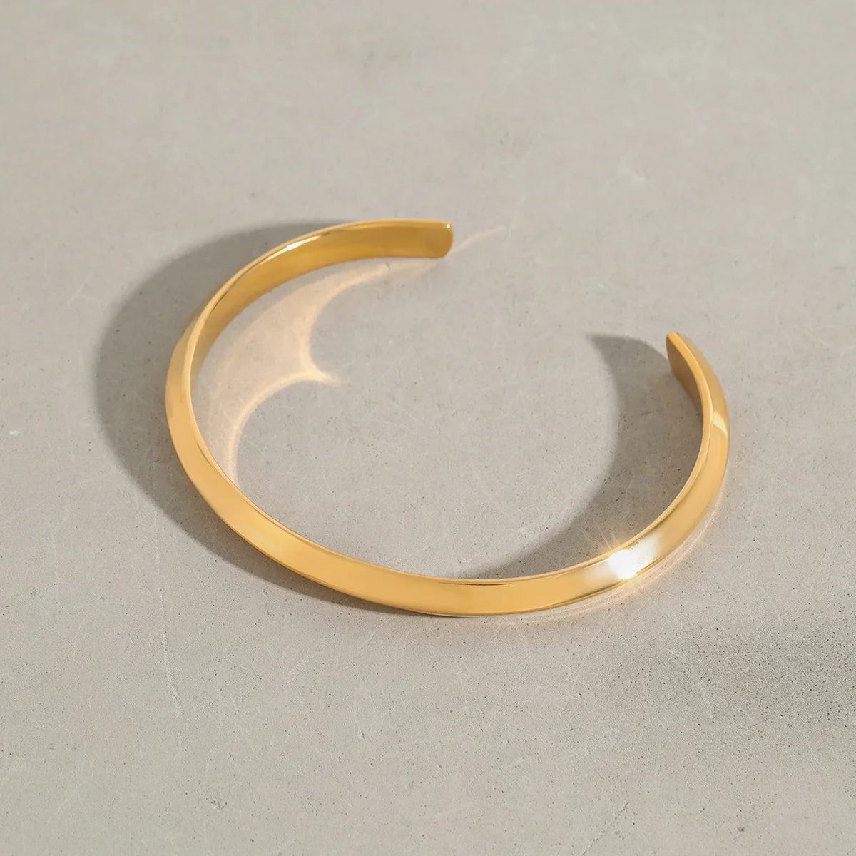 Polished gold sculpted open cuff bracelet from OROR Parure displayed on a neutral stone background.