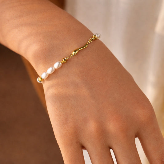 Gold and pearl-effect sculpted bracelet on wrist, minimal gold-plated details with pearl-effect beads