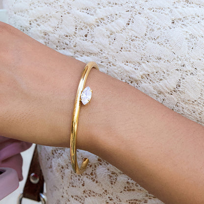 Open gold cuff with marquise-cut clear zircon on wrist, minimalist stacking style