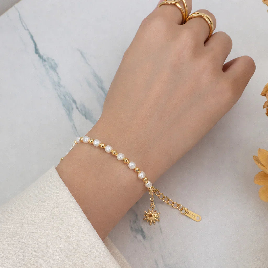 Sun charm bracelet on wrist with pearl-effect beads and gold chain links