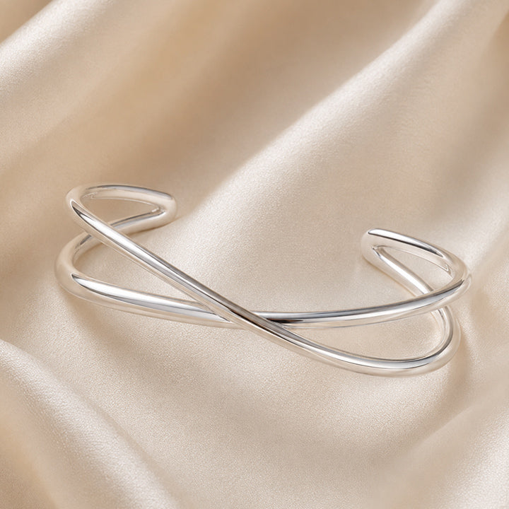 Polished silver crossover cuff bracelet on ivory satin background