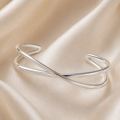 Polished silver crossover cuff bracelet on ivory satin background