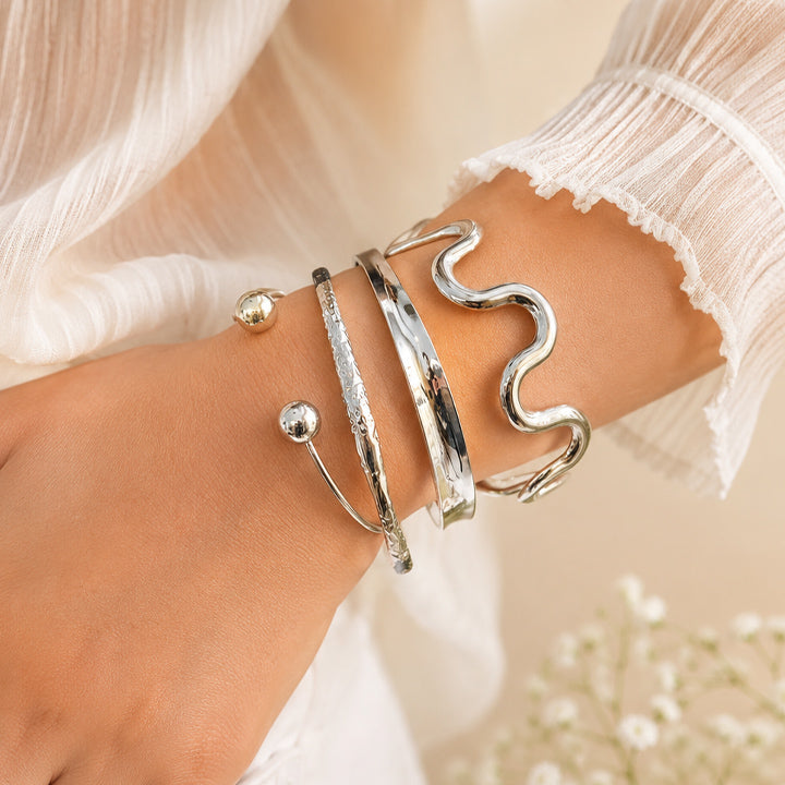Close-up of a wrist wearing multiple silver bracelets with a soft background